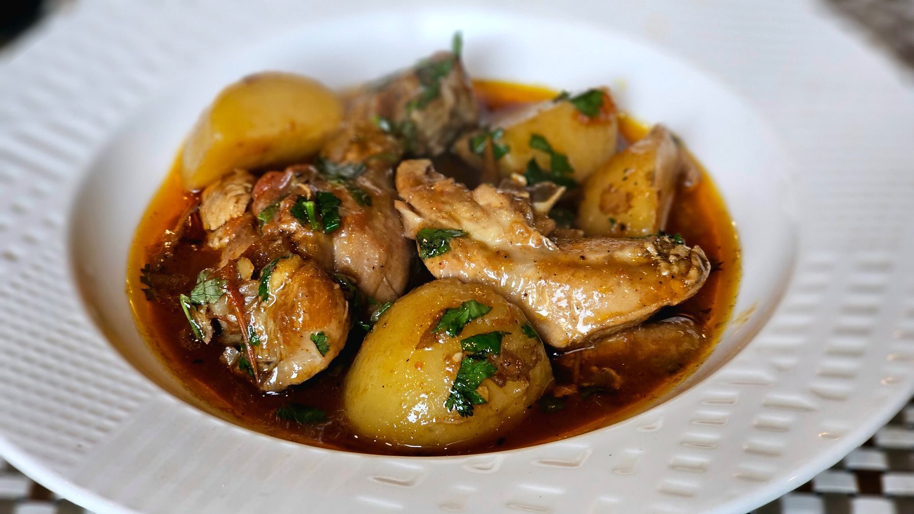 Chicken braised in a glossy caramel sauce, potatoes alongside, on a white plate